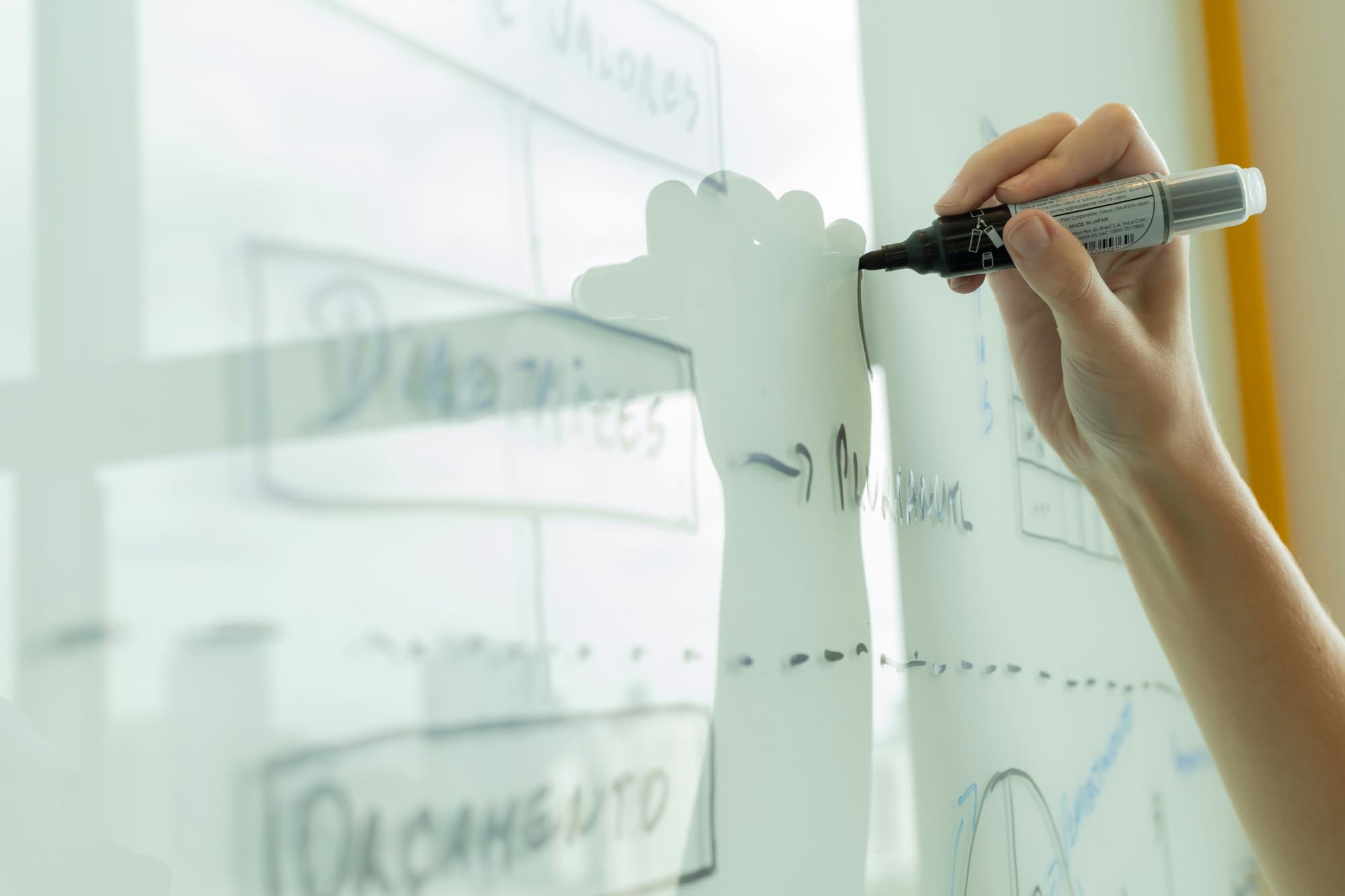 A person mapping out a plan on a glass wall with a marker
